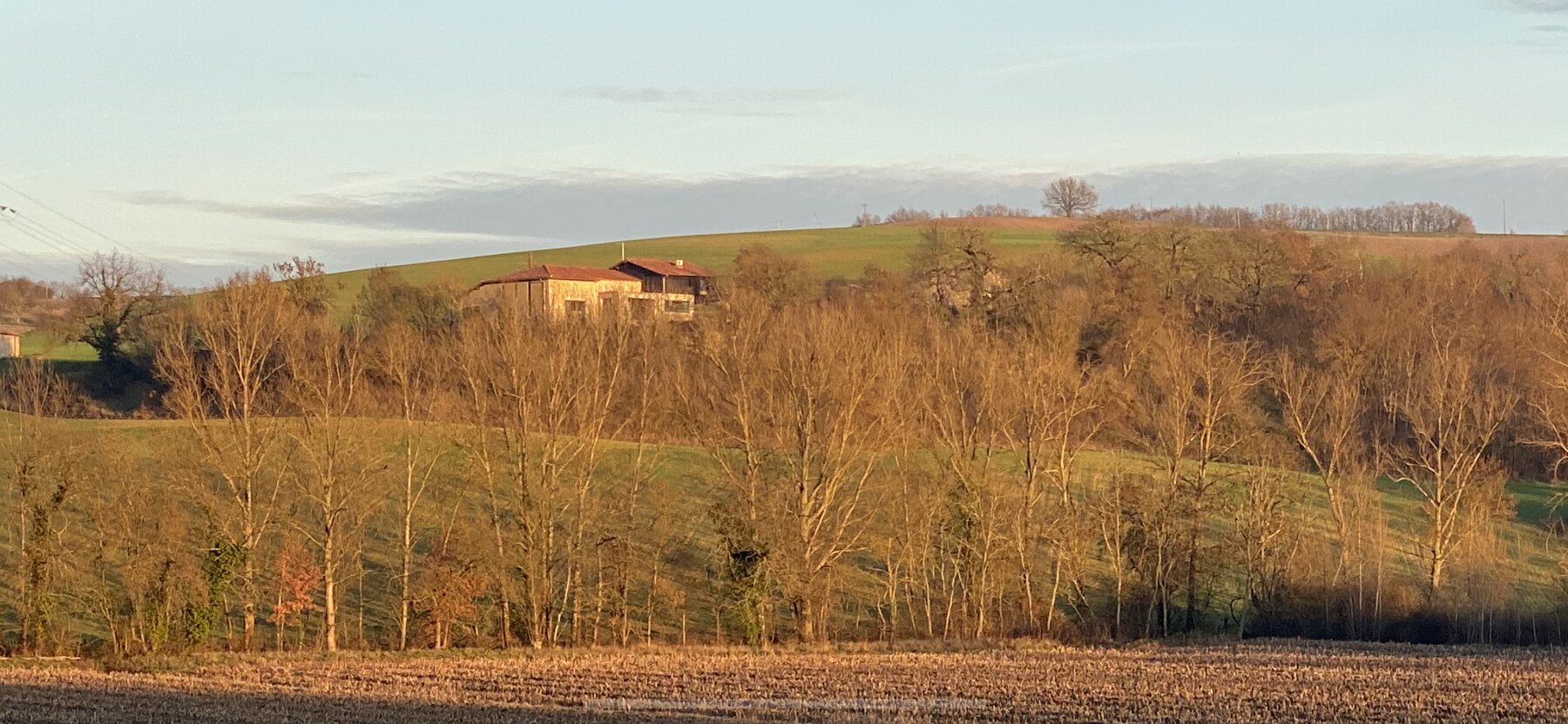La grange en pierre perchée sur sa colline, au milieu des coteaux boisés d'Occitanie, en lumière dorée