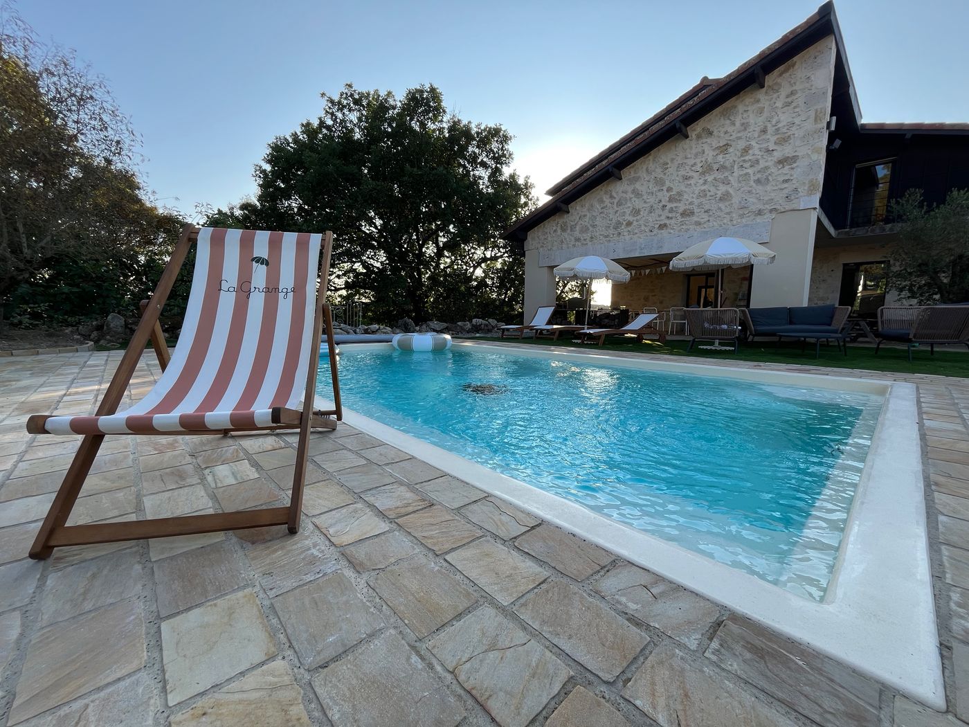 Une chaise longue rayée au bord de la piscine, dallage de pierre et grand ciel bleu