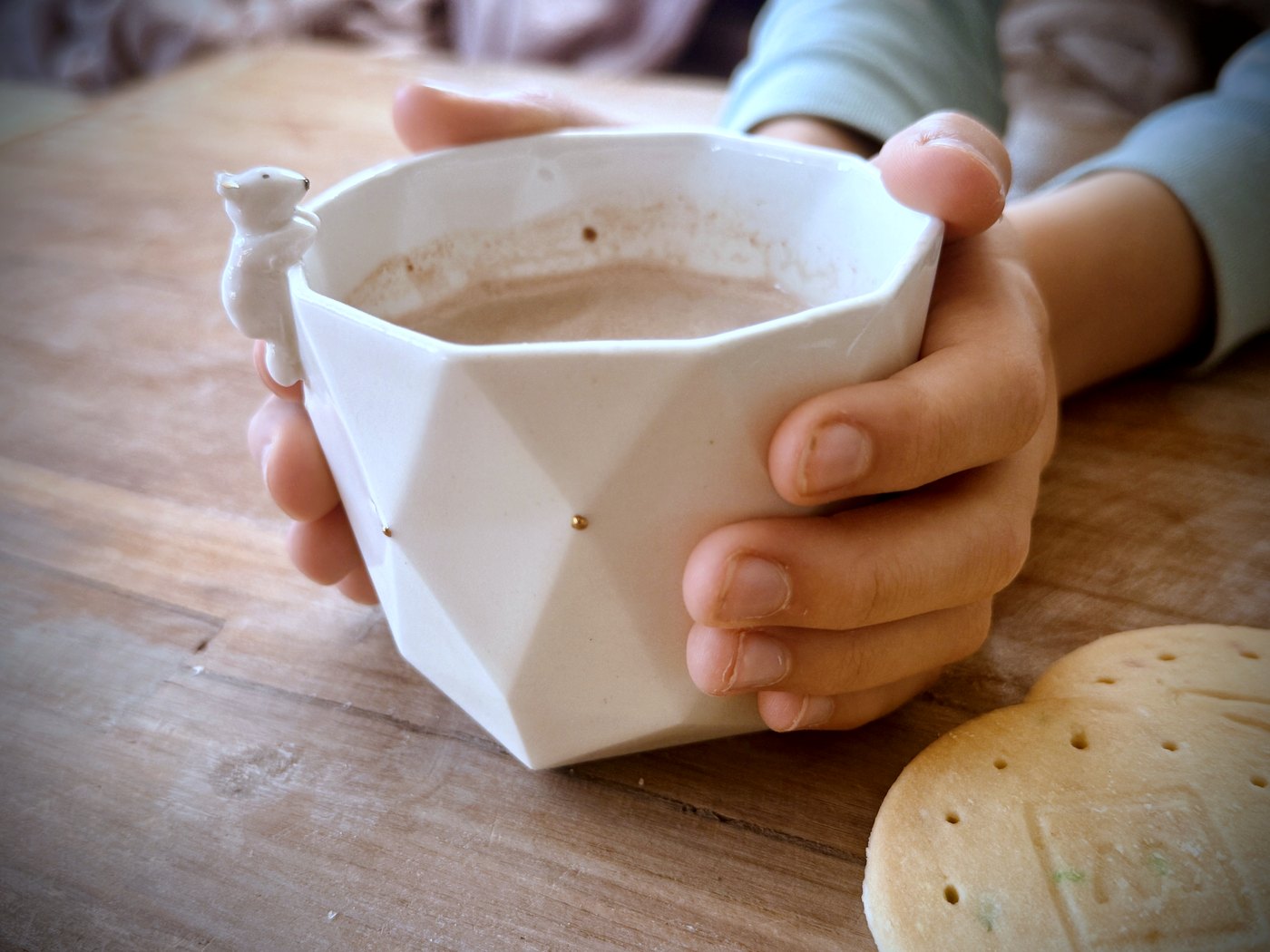 Petites mains d'enfant tenant une tasse de naissance en porcelaine faite main, ornée d'une figurine et d'une touche d'or